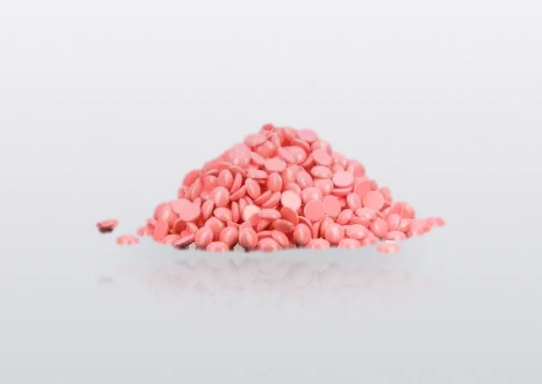 Rose pink consumer-grade hard wax beans in a loose pile on a white studio surface — the stock shade