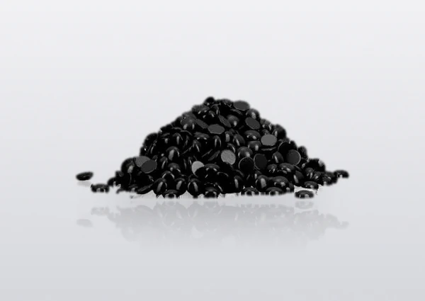 Custom black hard wax beans in a loose pile on a white studio surface — an optional shade of the same bead