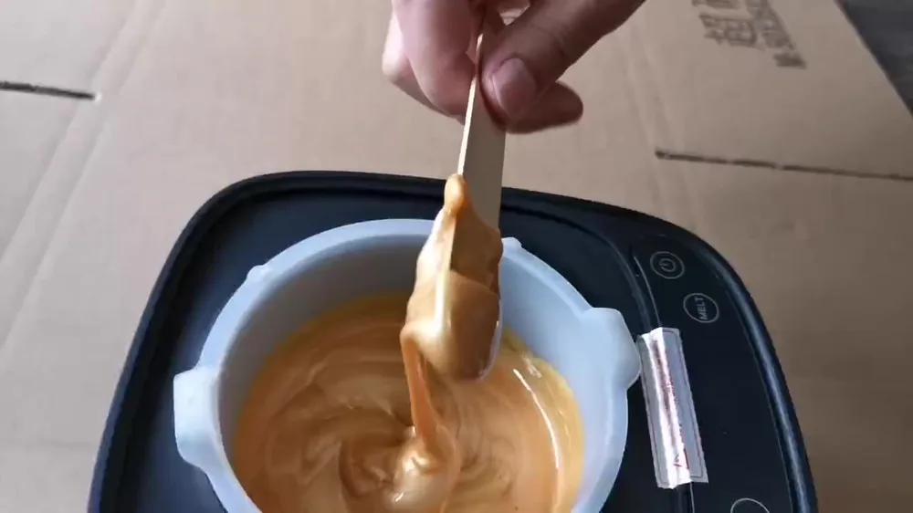 Molten gold hard wax stringing off a wooden spatula