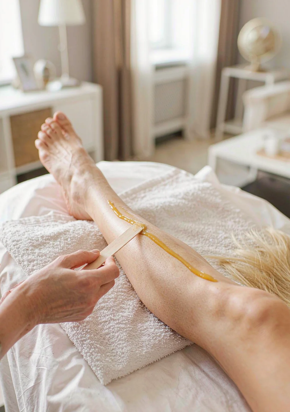 Golden hard wax being spread on a leg with a wooden spatula