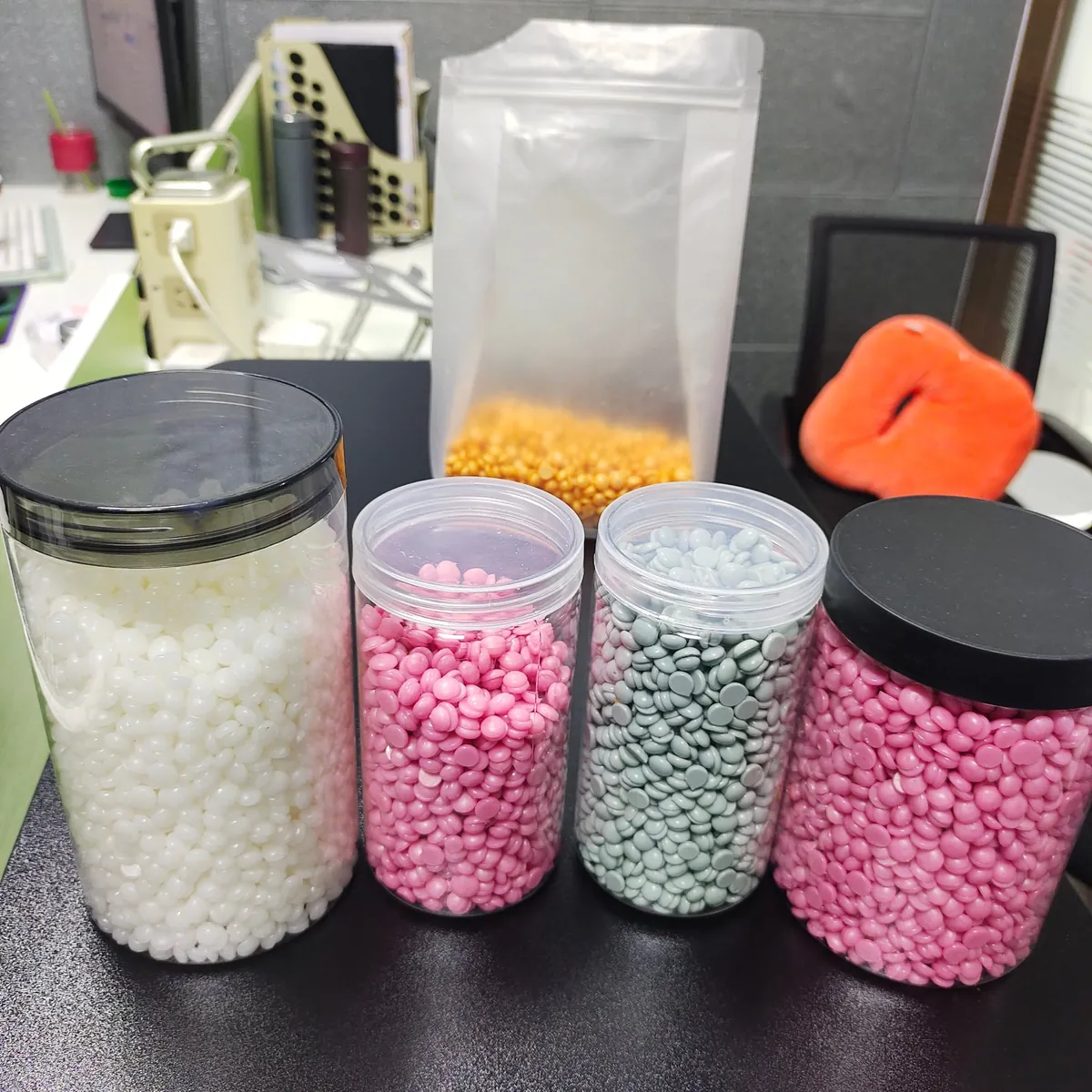 Four jars of consumer hard wax beans in different shades on the BeauTome studio bench
